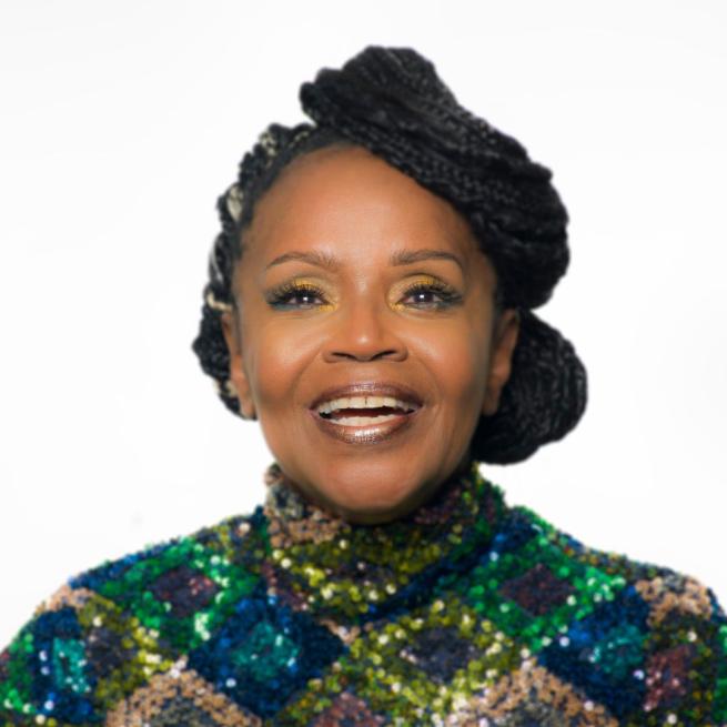 PP Arnold wearing a green sequin top smiling at the camera on a white background.