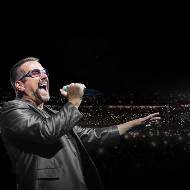 George Michael singing on stage into a hand-held microphone with the lights of an arena audience in the background.