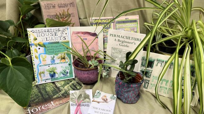 Zines surrounded by lots of green plants in front of a green fabric background