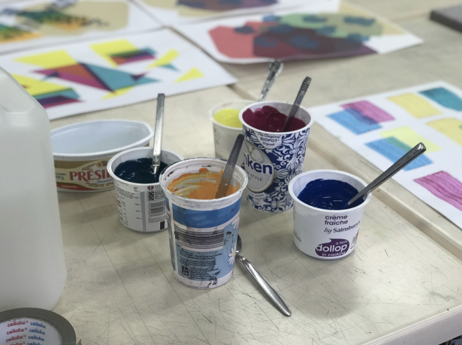 Different coloured inks in old yoghurt pots, surrounded by multi-coloured screen prints