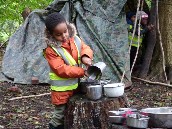 Photo of a boy playing in the mud kitchen in the woods.