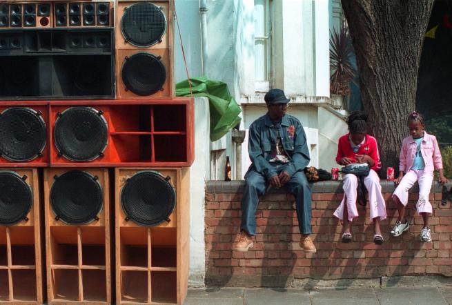 Young family sat on wall in residential street next to huge sound system PA