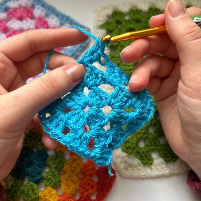 two hands crocheting a granny square with bright blue yarn