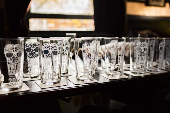 A bar full of pint glasses with the Pint of Science mascot on, which is a brain with glasses in a pint glass. 
