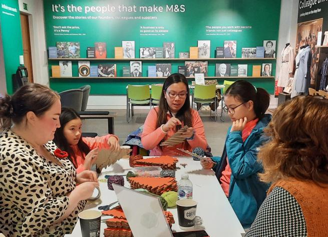 A colour photo of a group of people doing a craft activity in a museum