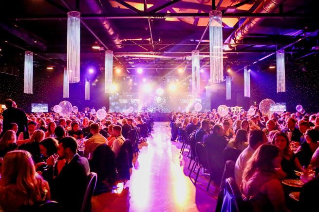 Guests seated at tables at a charity ball. A stage is in the background