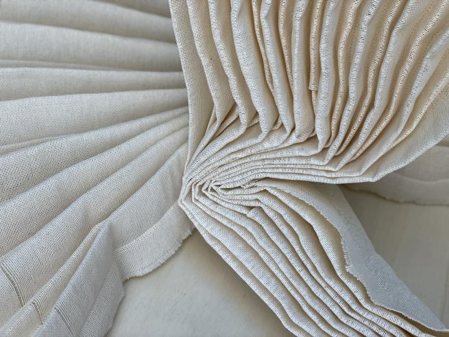 A piece by Hannah Robson with cream woven paper of pleats that concertina down onto a light wooden plinth.  