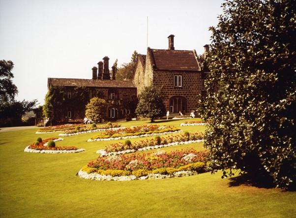 A colour photograph of some gardens and a house