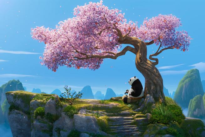 A panda meditates in front of a cherry blossom tree on a mountain.