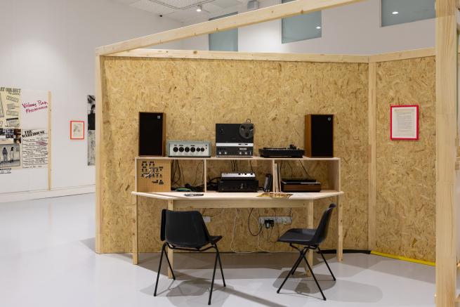 Analogue sound equipment against a wall constructed of chipboard within a white gallery space