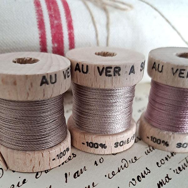 Image shows three spools of silk thread in muter colours on top of a hand written letter.