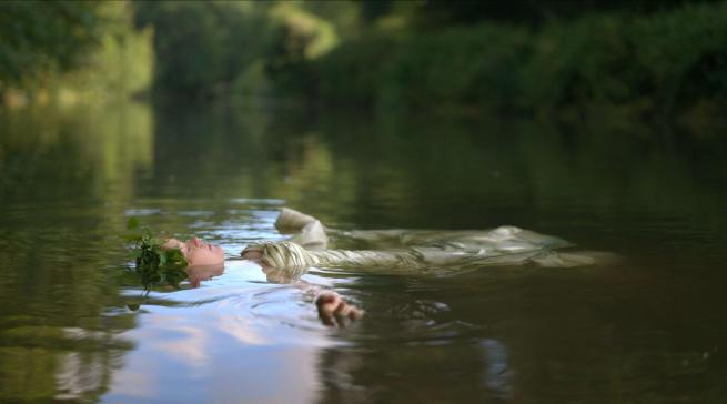 A woman is pictured floating in the river, face up. Peaceful. Trees can be seen in the rear of the frame. 