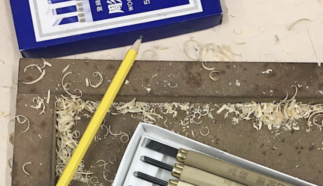 Woodcut tools and a pencil, surrounded by wood shavings