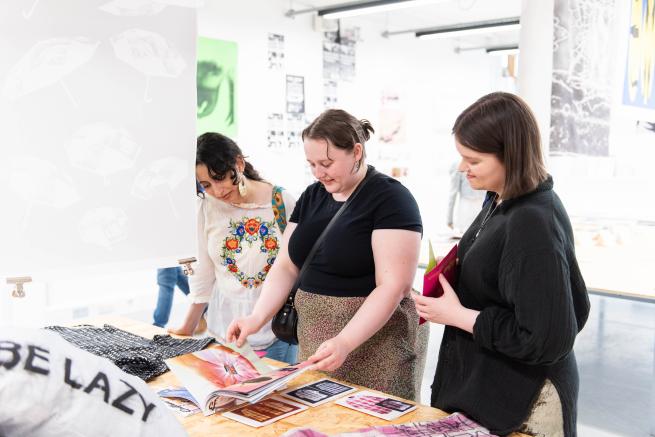 People looking at printed books made by students in a studio