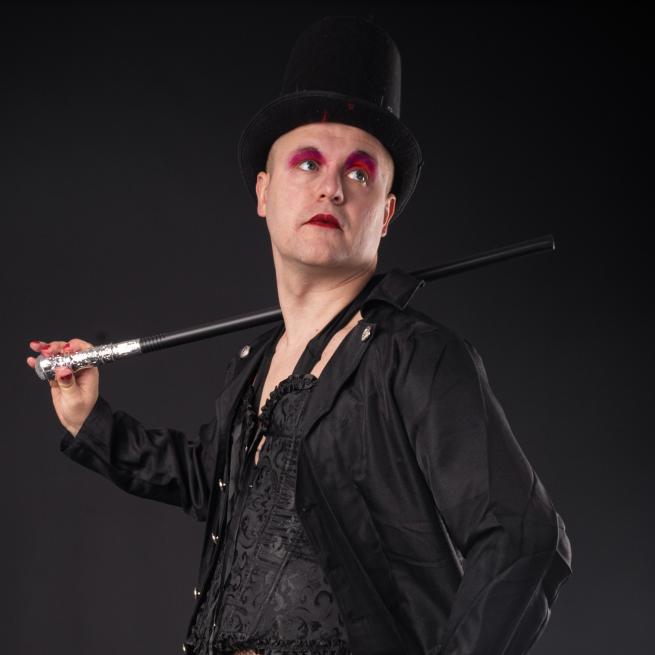 A man wearing red eye makeup dressed in black with a top hat and a cane over his shoulder.