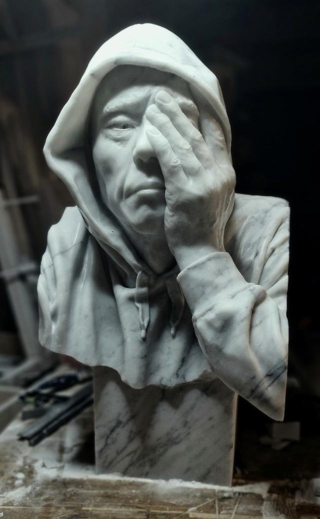 A hooded male figure covers one eye with his hand with an expression of despair