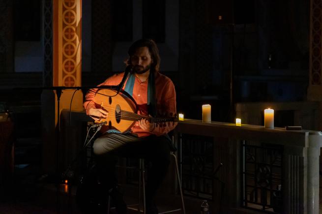 Dim lights surround Ibantuta playing oud live during his show in a chapel surrounded by candles providing an intimate atmosphere