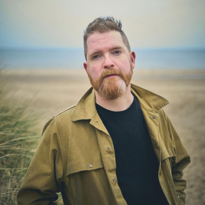 John Smith stood in front of a beach with the shoreline blurred behind him.