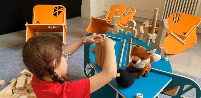Young person playing with wooden blocks amidst rocking chairs