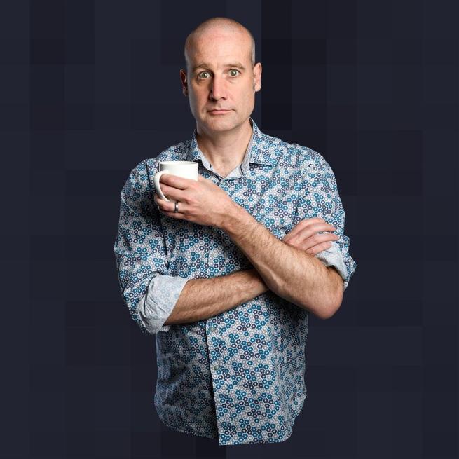 Matt Parker wearing a blue short-sleeved shirt with his arms crossed holding a mug in his right hand.