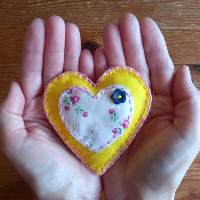 cupped hands holding a yellow felt love heart with applique embelishments