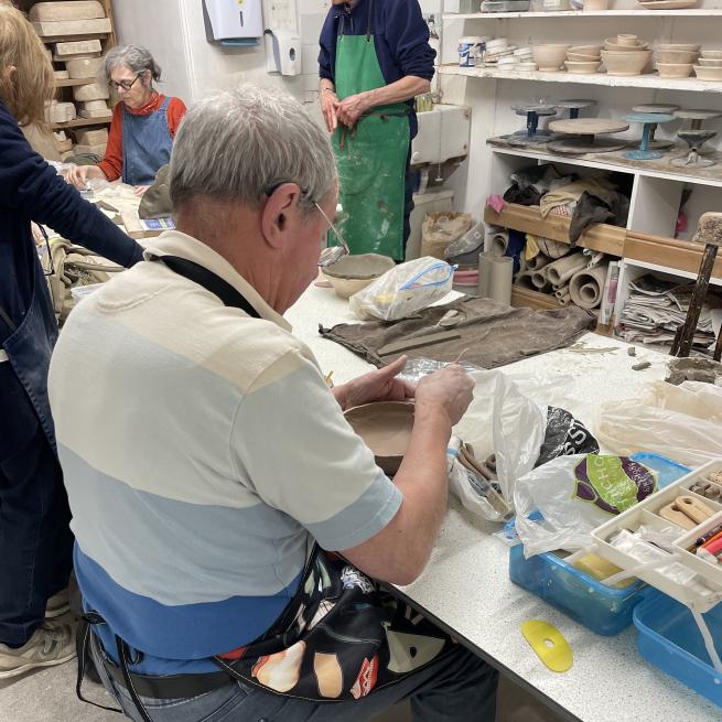 An older man sat at a table smoothing out a ceramic bowl