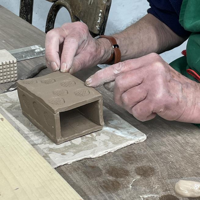 two hand touching a box form made from brown clay
