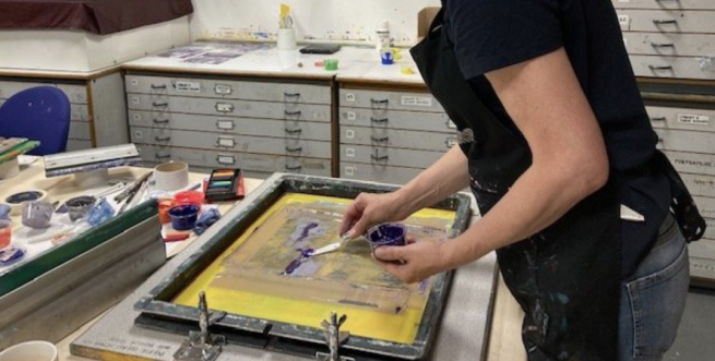 A person preparing a printing screen with purple ink