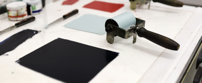 Black, blue and red ink rolled onto a surface, with an inking roller and other printing tools.