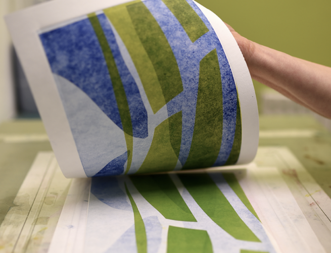 An abstract monoprint being revealed in shades of green and blue
