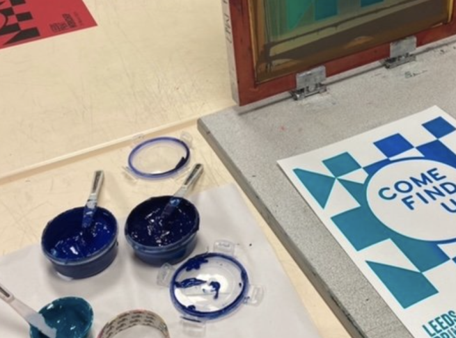 A printing screen with blue inks being used to print a graphic poster design