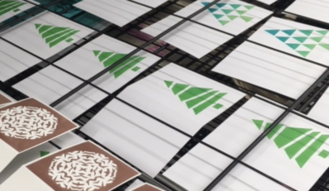 Screen printed Christmas cards with designs featuring snowflakes and Christmas trees arranged on a drying rack
