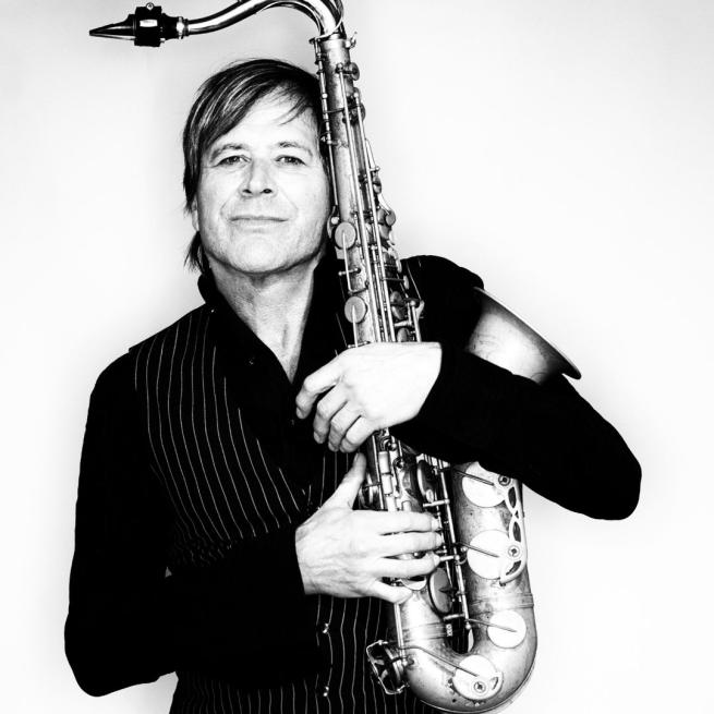 Steve Norman in black and white hugging a saxophone.
