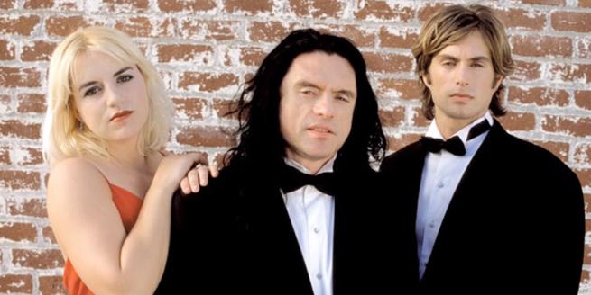 Three people, two men in suits and one woman in a red dress face the camera. 