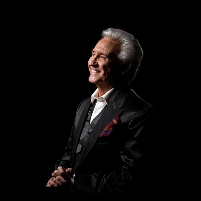 Tony Christie in a patterned suit smiling and facing to his right.
