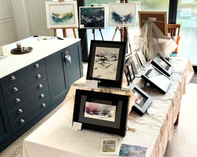 A kitchen table showing framed paintings by Rachel Bentley Artist in multiple sizes and colours