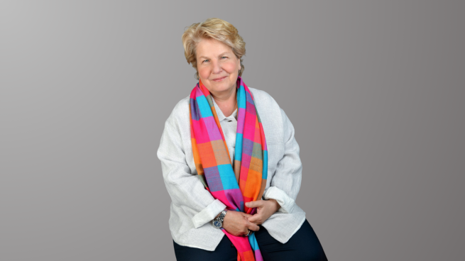 A person with short blonde hair sat on a chair wearing a colourful scarf. 