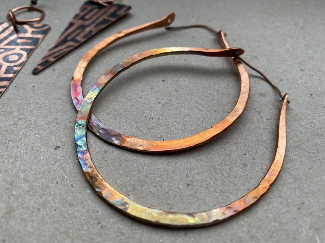 A pair of copper hoop earrings made by Amanda Burton. The copper has been torched so the metal has a rainbow of colours.