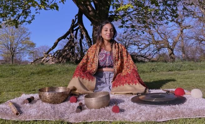 Neeta sits peacefully cross-legged under a tree surrounded by singing bowls