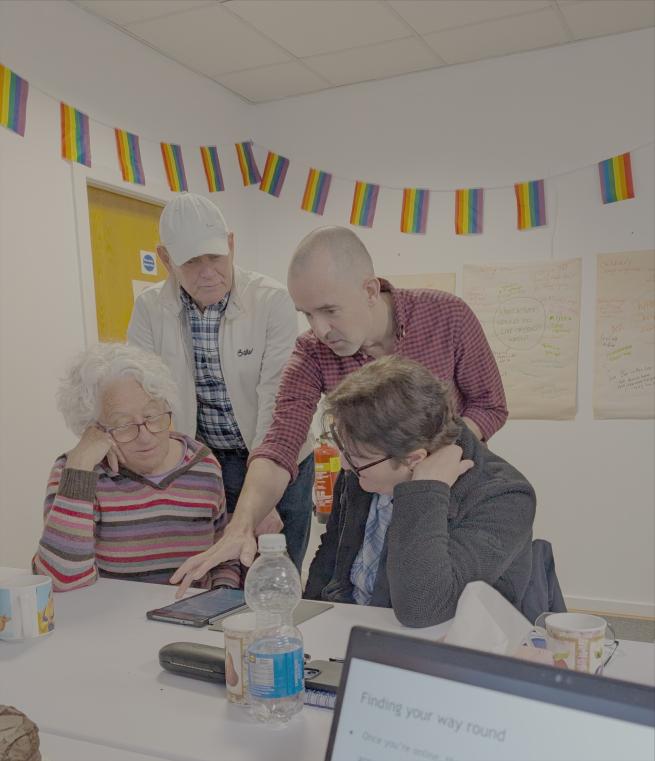 four people gathered around a tablet co-working at Pride Place