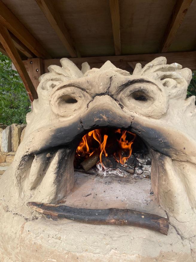 A wood-fired pizza oven in the shape of a dragon's head. There are flames in its mouth.