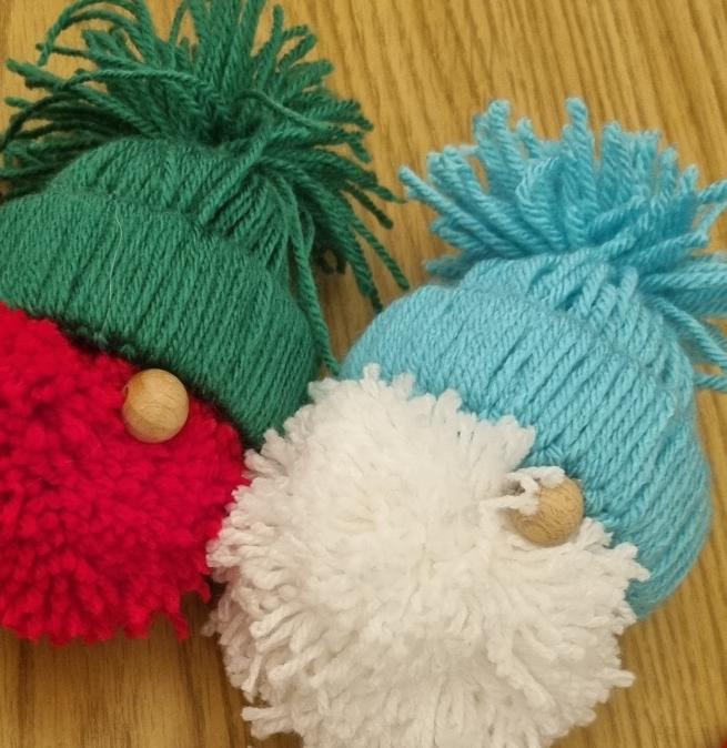 A picture of two pom pom gnomes. One has a red face and a green hat, the other has a white face and a turquoise hat