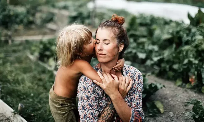 A child has their arms wrapped around a woman, and is kissing her on the cheek.
