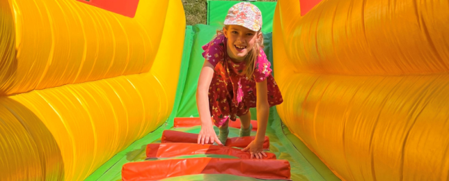 teenage girl climbing up a yellow, green and red inflatable slide