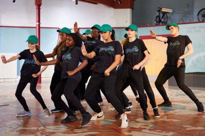 TEMPO members in black t-shirts and turquoise hats dance in formation