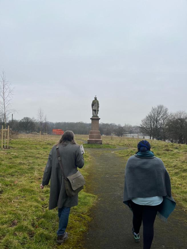 Heritage walkers on Monument Moor in Leeds, walking towards the statue of Henry Rowland Marsden. A seagull is sitting on the statue's head.
