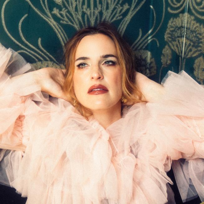 Singer-songwriter Juliet Lloyd in a pink tulle top, posing against an ornate green backdrop.
