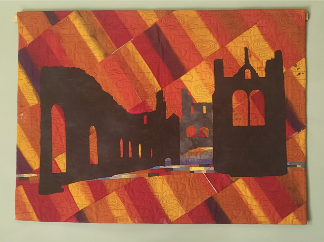 A textile piece with quilted red and orange fabric in the background and the silhouette of an abbey in deep brown
