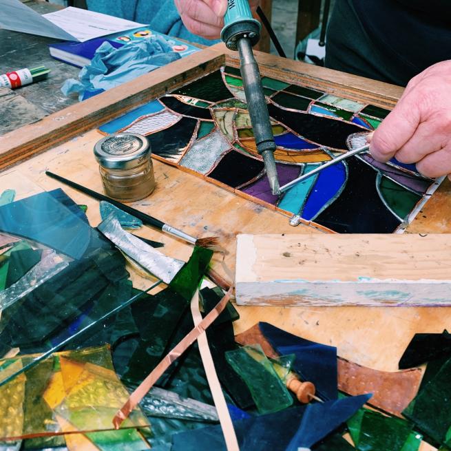 Two hands soldering a blue toned stained glass piece