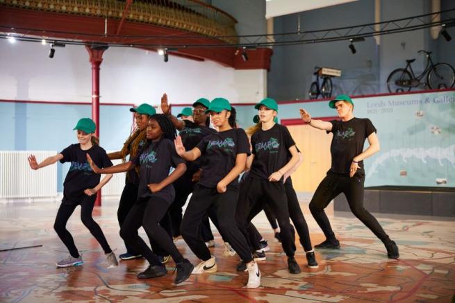 TEMPO members in black t-shirts and turquoise hats dance in formation